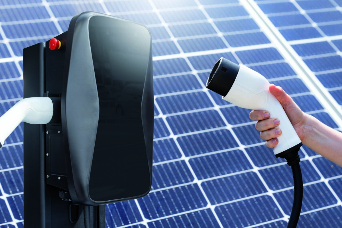 Hand with electric vehicles charging plug on a background of solar panel.